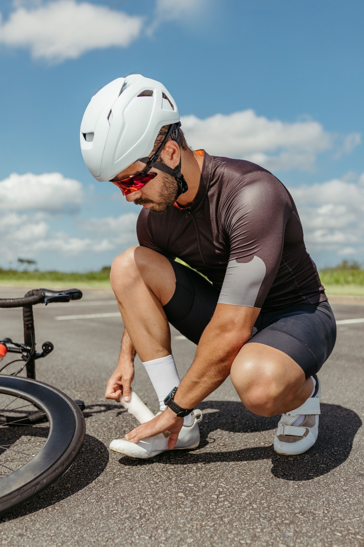 Radfahrer kniet auf der Straße, richtet seine Schuhe.