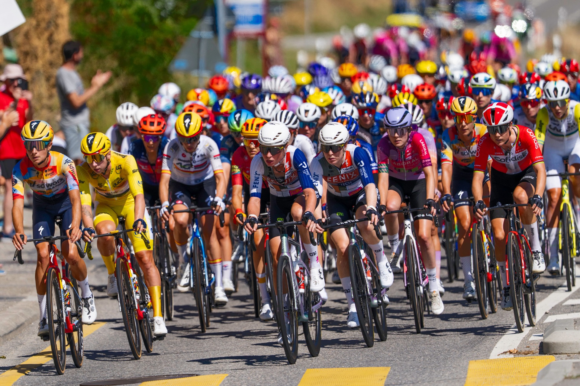 Große Gruppe Radrennfahrerinnen im Peloton der Tour de Frances Femmes, enge Formation auf der Straße, Helme und Teamtrikots in der Sonne.